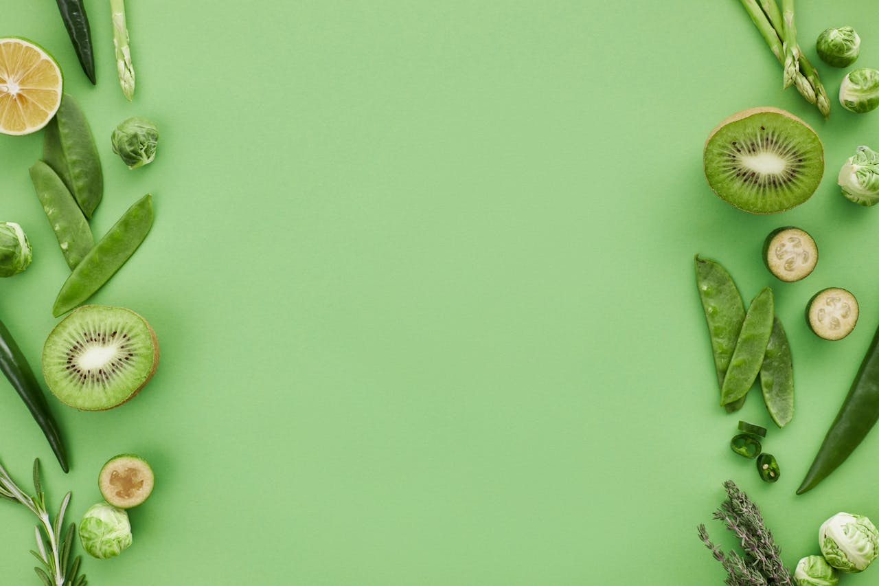 Fresh assortment of green fruits and vegetables arranged with ample copy space on a green background.