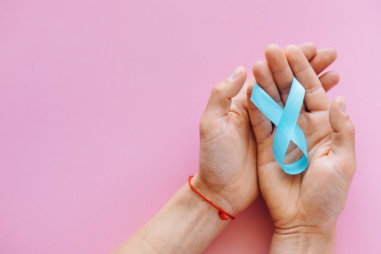 Hands holding a blue ribbon on a pink background symbolizing awareness and support.